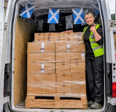 Worker standing beside packed boxes in a van decorated with Scottish flags.