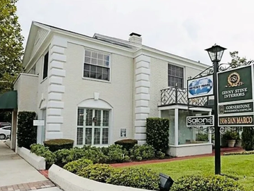 White two-story building housing multiple businesses with signage outside.