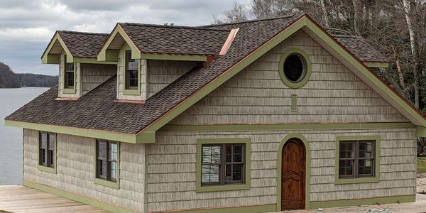 A quaint lakeside cabin with green trim and a wooden deck.