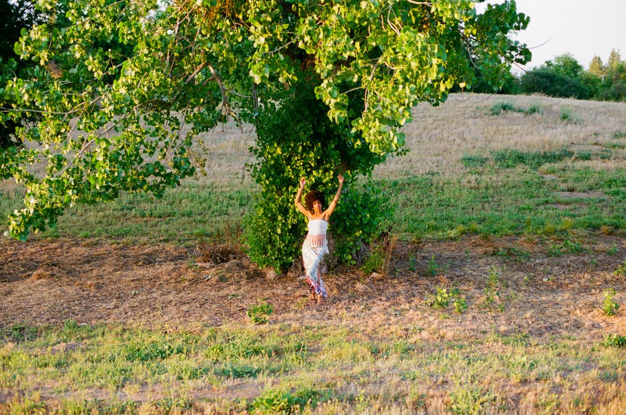 Woman standing under a large green tree in a field.