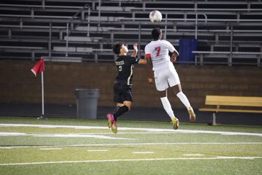 Two soccer players jump to head the ball during a match on the field.