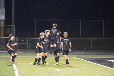 Soccer players celebrating a goal on a lit field at night.