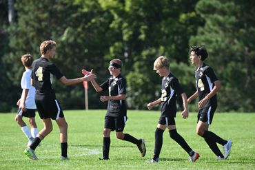 Youth soccer players celebrating on the field in black uniforms.