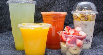 Colorful fresh fruit juices and fruit cups in plastic containers.