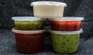 Five plastic containers filled with different sauces and dips.