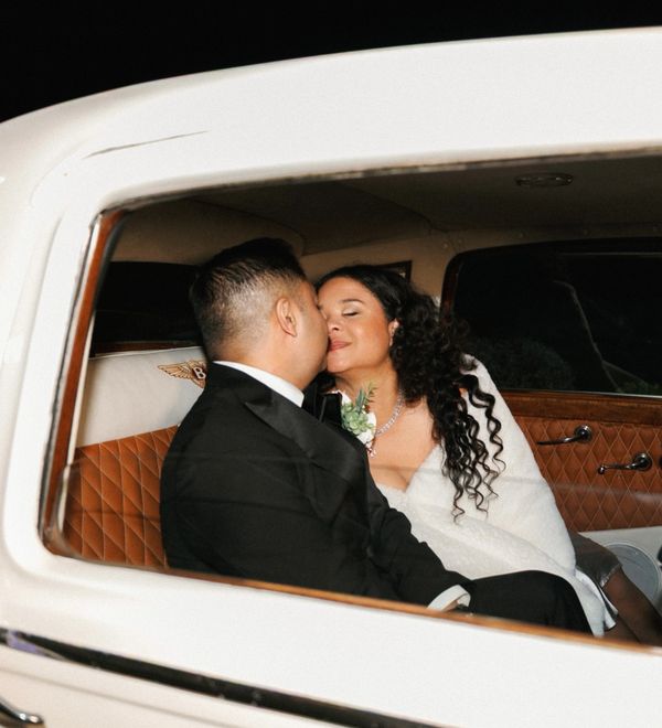Newlyweds sharing a tender moment inside a luxurious car after their wedding.