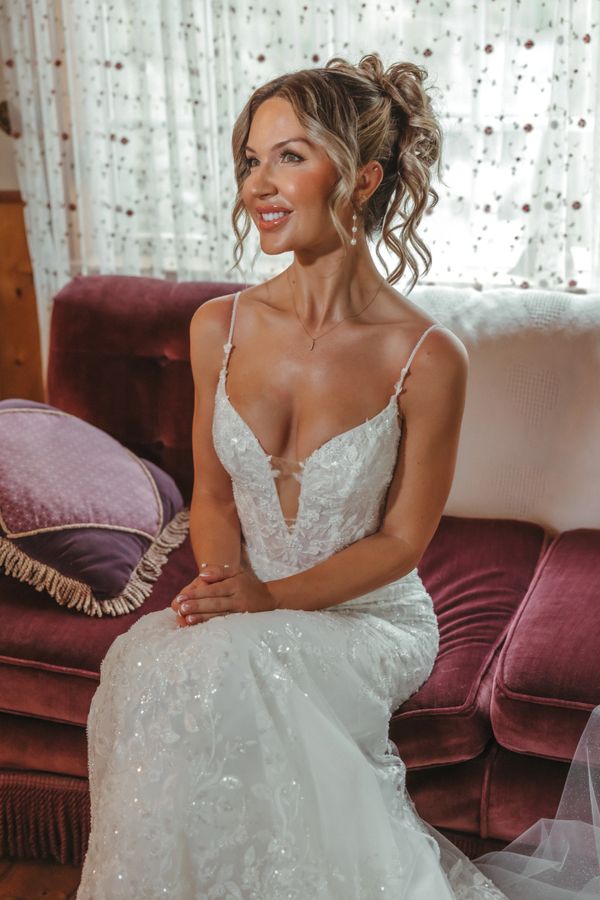 Bride in elegant lace wedding dress sitting on a plush velvet couch.