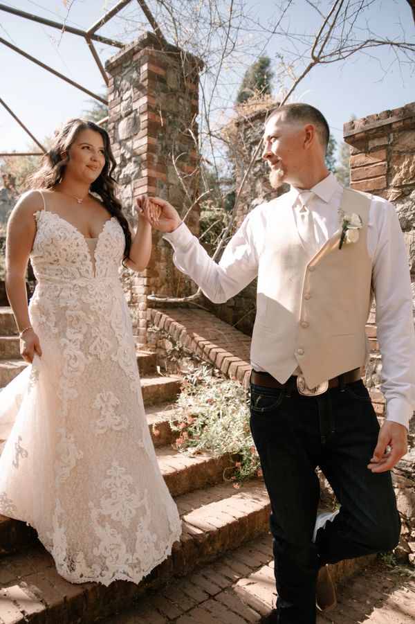 Bride and groom holding hands on rustic stone steps outdoors.