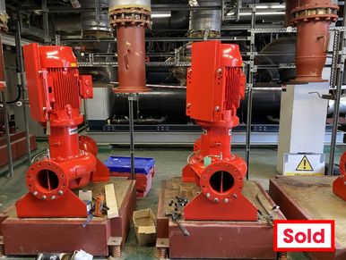 Two red industrial pumps installed in a factory setting.