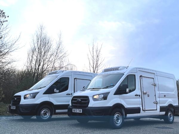 Edited image of two white refrigerated panel vans sitting in a yard vans parked to the side