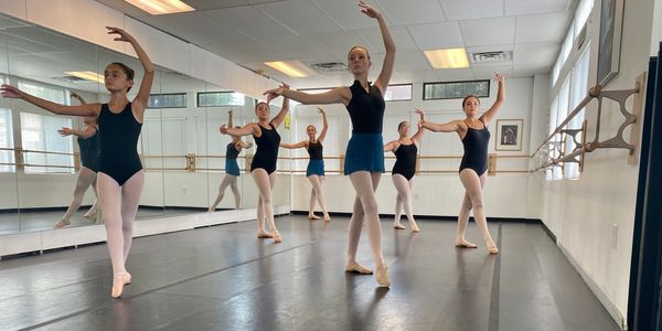Young ballet dancers practicing in a dance studio wearing black leotards and pink tights.