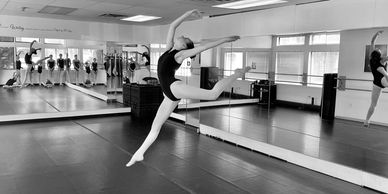 A ballet dancer leaps gracefully in a mirrored dance studio.