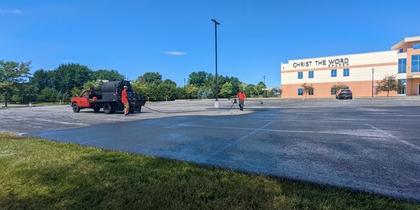 asphalt sealcoating being sprayed from a red truck on a huge church parking lot
