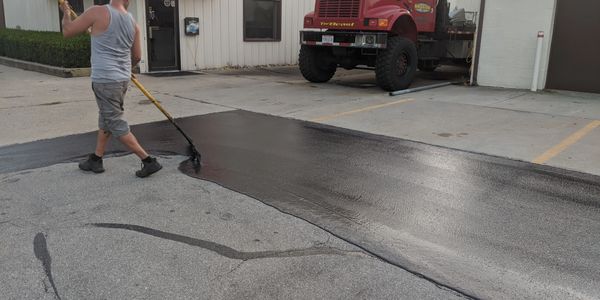 Sealcoating in progress: Small parking lot being resurfaced with a tow truck parked nearby.