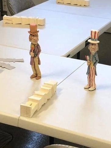 Two Uncle Sam figurines stand on a table surrounded by dominoes.