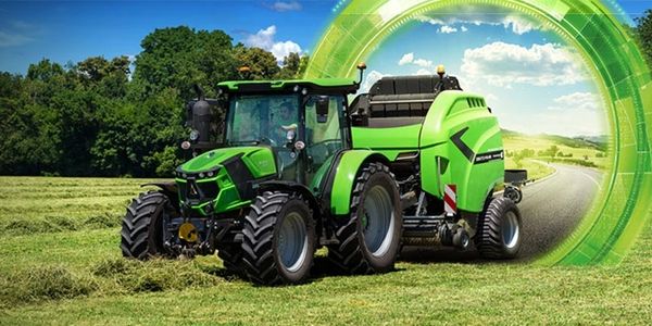 A green tractor working on a field under a blue sky.