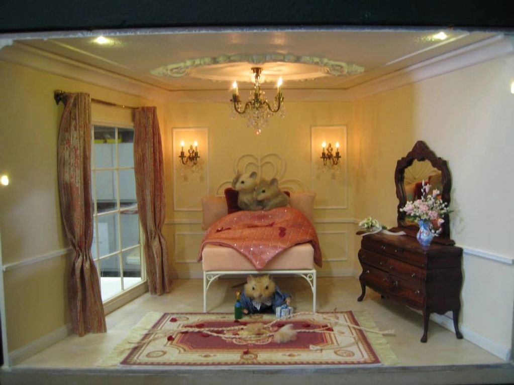 Image of miniature bedroom, a pair of mice in bed, looking out window.  Another mouse underneath.  