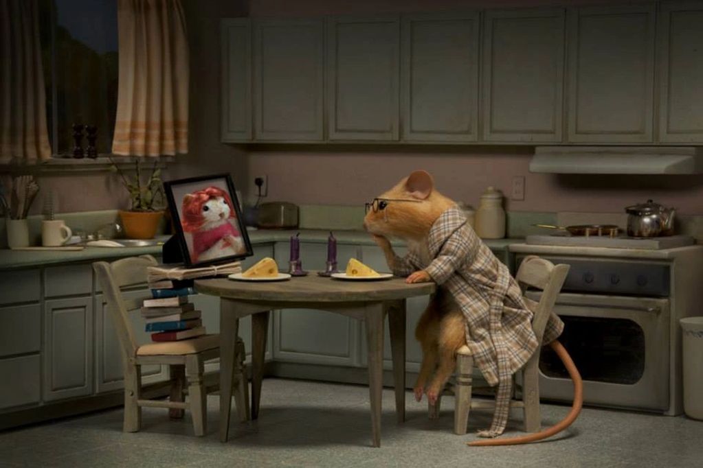 Image is a miniature kitchen with a mouse looking at a photo, with plates of cheese on the table.