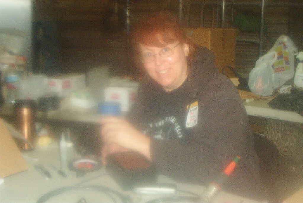 Image shows blurry photo of smiling woman at a workbench.