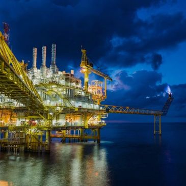 Illuminated offshore oil rig at night with dark cloudy sky.