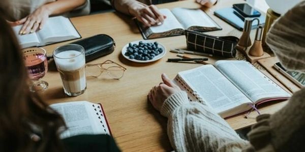 People studying with books and coffee at a wooden table.