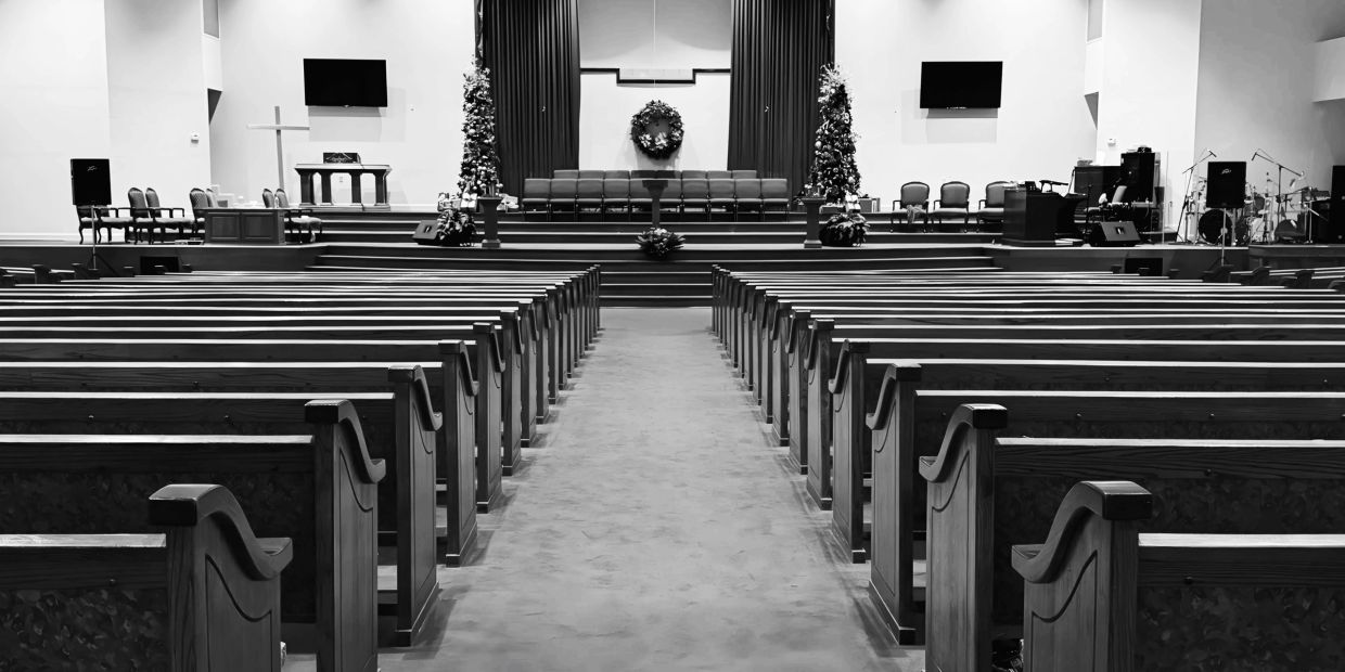 Empty church interior with rows of wooden pews and a decorated altar.