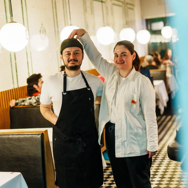 Two restaurant staff posing playfully in a warmly lit dining area.