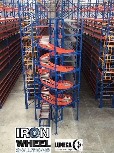 Spiral conveyor system inside an industrial warehouse with metal shelving.