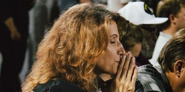 Woman with curly hair praying with eyes closed in a crowd.