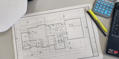 residential blueprints on a table with construction hat, pens, highlighters and calculators