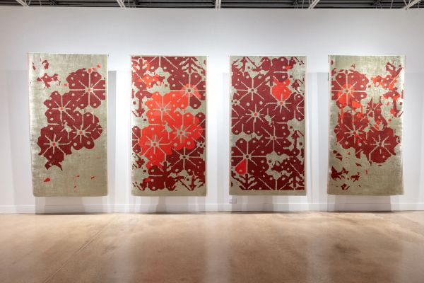 Four abstract patterned rugs with red and orange designs displayed in a gallery.
