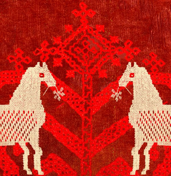 Two white horses facing each other on a red textile with intricate patterns.