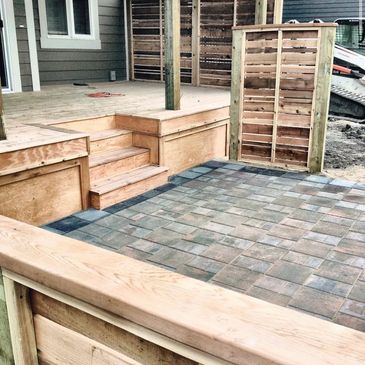 Newly constructed wooden deck and stone patio in a backyard.