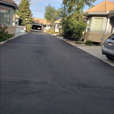 Newly paved asphalt road in a residential neighborhood with houses on both sides.