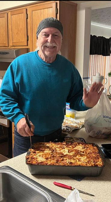 Smiling man in a blue sweater with a large homemade lasagna.