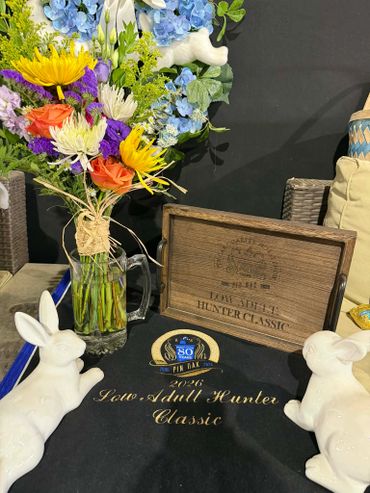 Floral arrangement with Lake Shelby Hunter Classic memorabilia and white rabbit figurines.