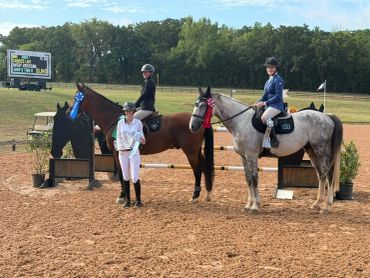 Three equestrians with horses in a riding arena during a competition.