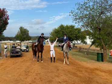 Three people and two horses on a dirt path celebrating.