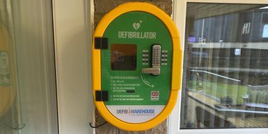 Wall-mounted defibrillator unit in a yellow and green case for emergency use.