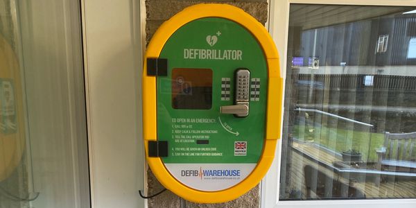 Wall-mounted defibrillator unit in a yellow and green case for emergency use.