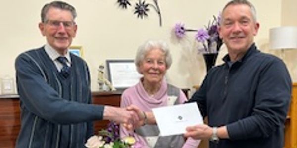 Three people exchanging a certificate in a cozy room with flowers.