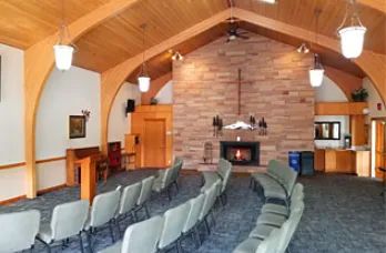 Interior of a small chapel with stone fireplace and rows of chairs.