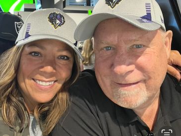 Smiling couple wearing matching light-colored baseball caps with logos.