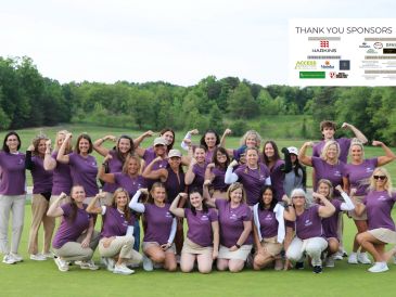 Group of women in purple shirts flexing muscles outdoors on golf course.