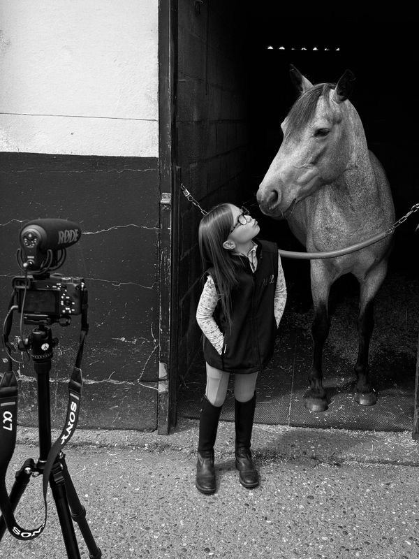 A girl and a horse share a moment in a stable while being filmed.