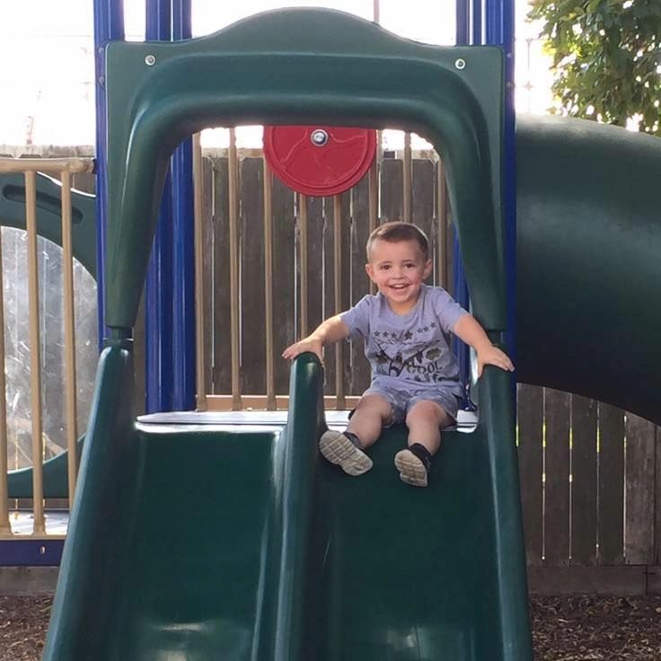 Happy boy sliding down a playground slide.