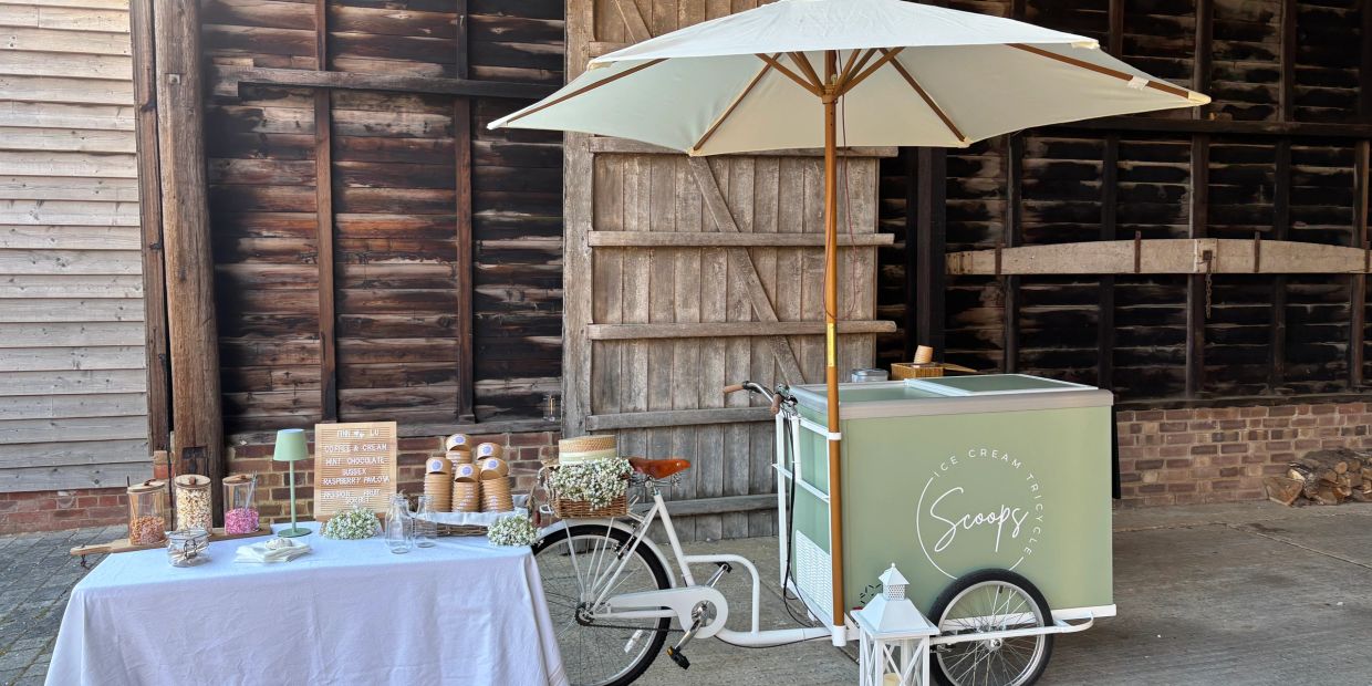 Ice cream tricycle with umbrella and a table set up in rustic barn.