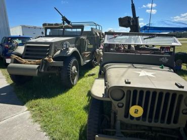 Two vintage military vehicles parked on grass under blue sky.