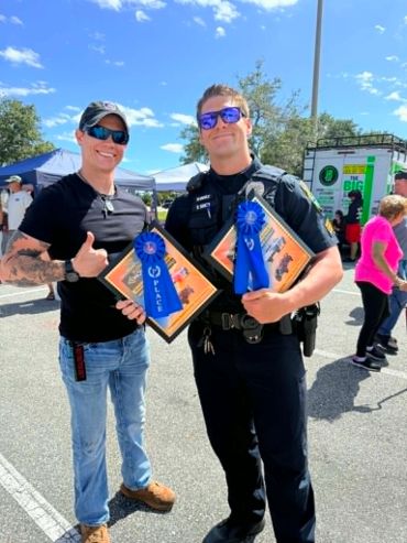 Two men holding 1st place awards at an outdoor event.