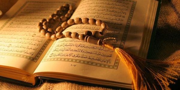 An open Quran with prayer beads resting on its pages in warm lighting.